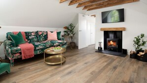A living room with a sofa, a round coffee table, a fireplace, and wooden beams on the ceiling.