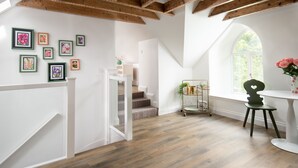 A spacious room with wooden beams, a staircase, and a window with a view of greenery.
