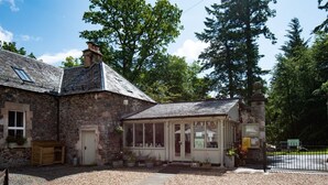 A stone building with a small shop, gravel driveway, and surrounding trees.