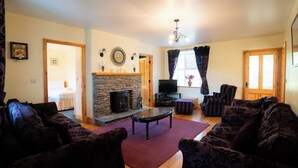 A living room with a stone fireplace, a television, and patterned furniture.
