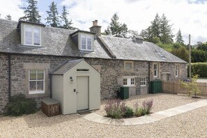 A stone house with a sloped roof, a small shed, and a gravel driveway.