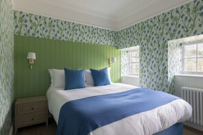 A bedroom with a green headboard, a bed with blue and white bedding, two bedside lamps, a nightstand, and a window with a view. - Coachman's Cottage, Kailzie - sleeping 4 guests in 2 bedrooms (Peebles)