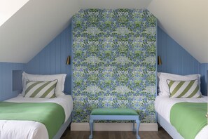 A bedroom with two beds, a bench, and a patterned wallpaper.
