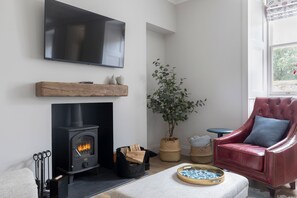 A living room with a fireplace, a television mounted on the wall, a red leather armchair, and a potted plant.
