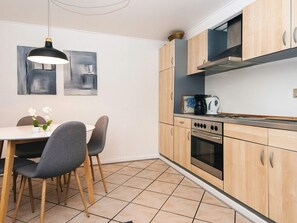 A modern kitchen with wooden cabinets, a stove, and a dining area with chairs and a table.