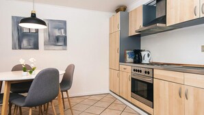 A compact kitchen with a dining area, featuring a modern stove, microwave, and a hanging light fixture. - 2 Person Holiday Home in Hojer (Højer)