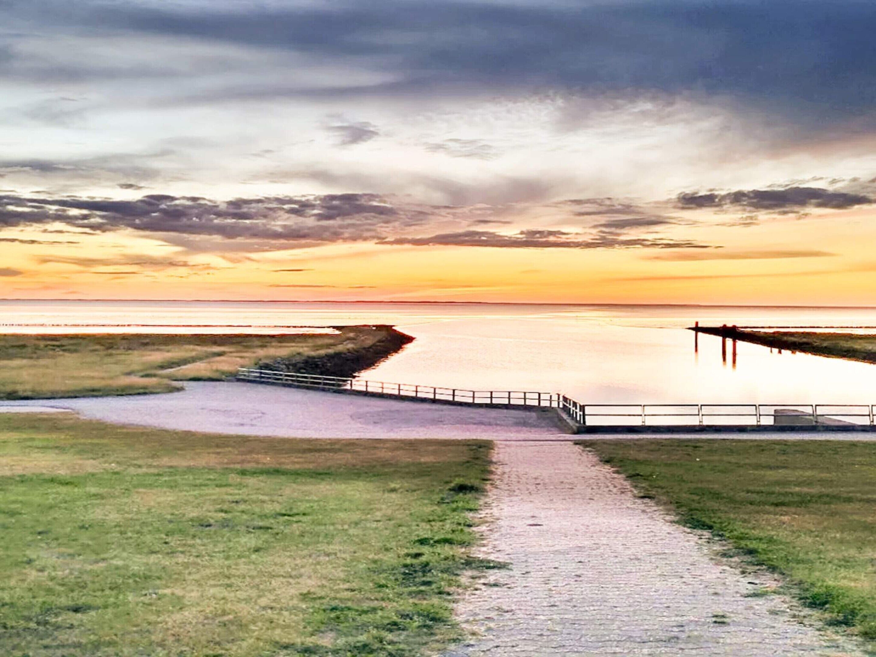 A coastal path leading to a pier with a view of the sea and a sunset.