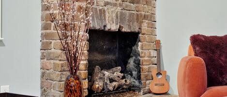 A fireplace with a brick wall, a guitar, and a vase with branches.