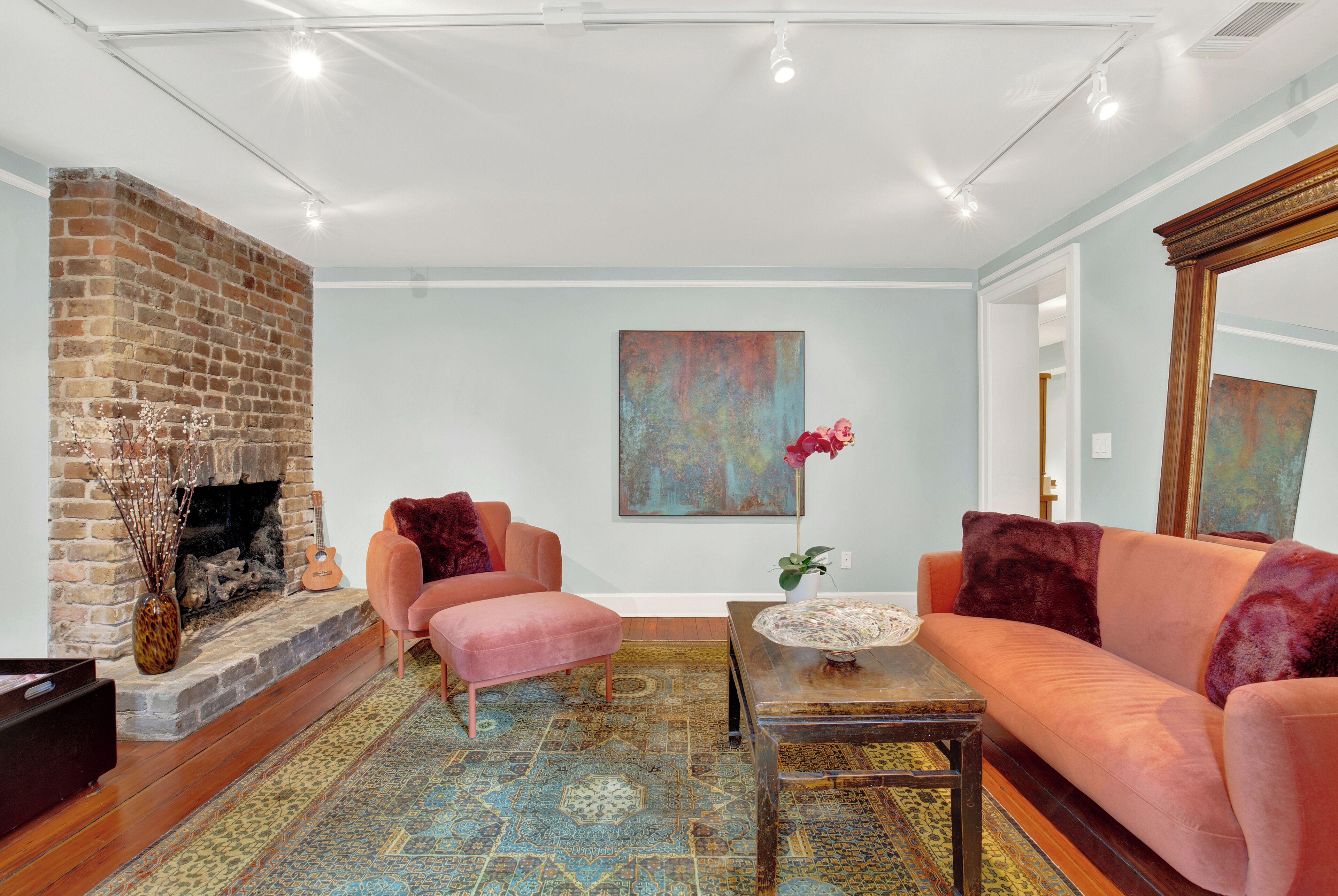A living room with a brick fireplace, a pink sofa, a patterned rug, and a large abstract painting on the wall.