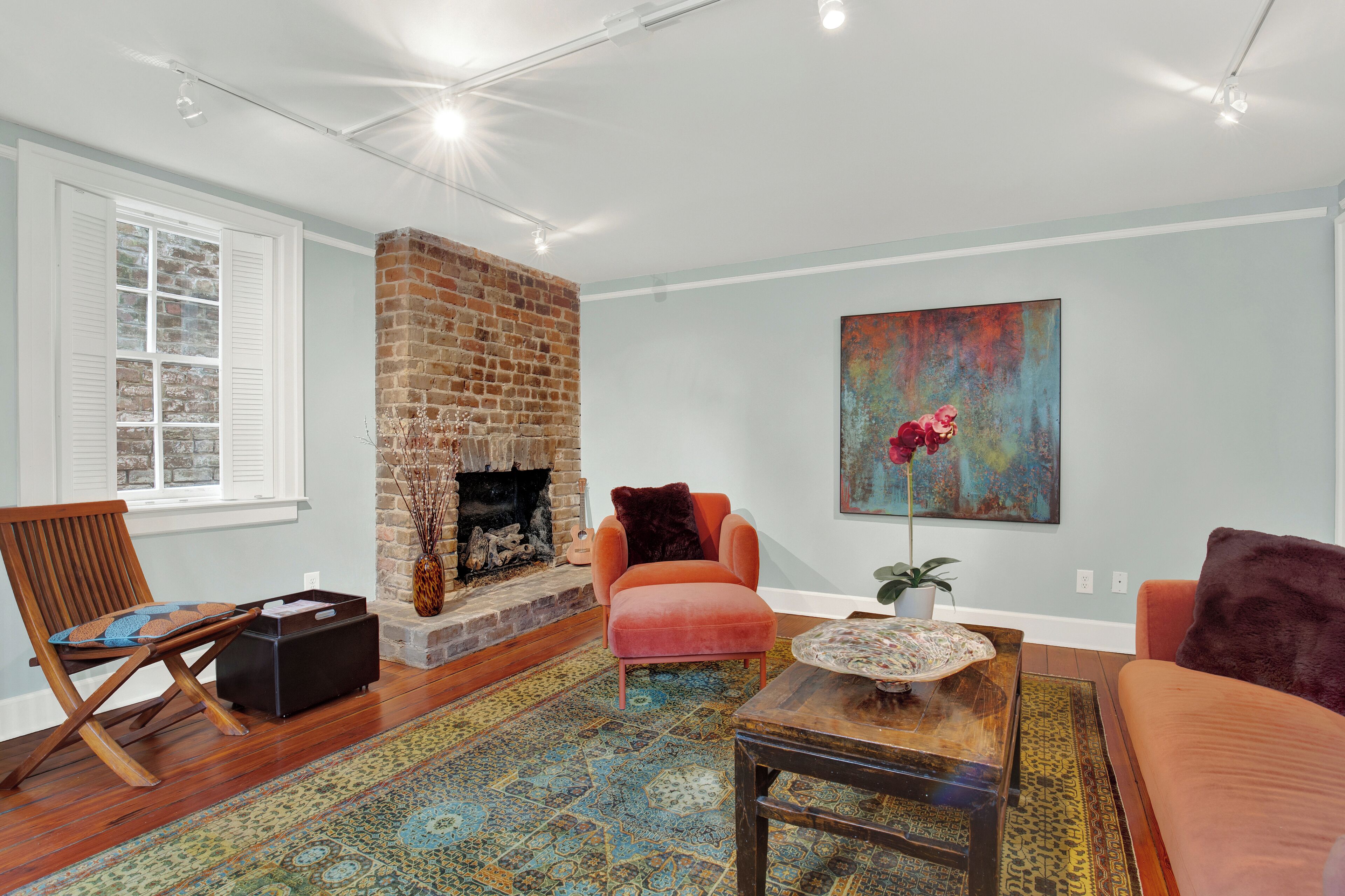 A living room with a brick fireplace, a colorful rug, and a large abstract painting.