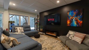 Ein modernes Wohnzimmer mit Kamin, einem großen Flachbildfernseher, der 'NETFLIX' anzeigt, und einem lebendigen abstrakten Gemälde.