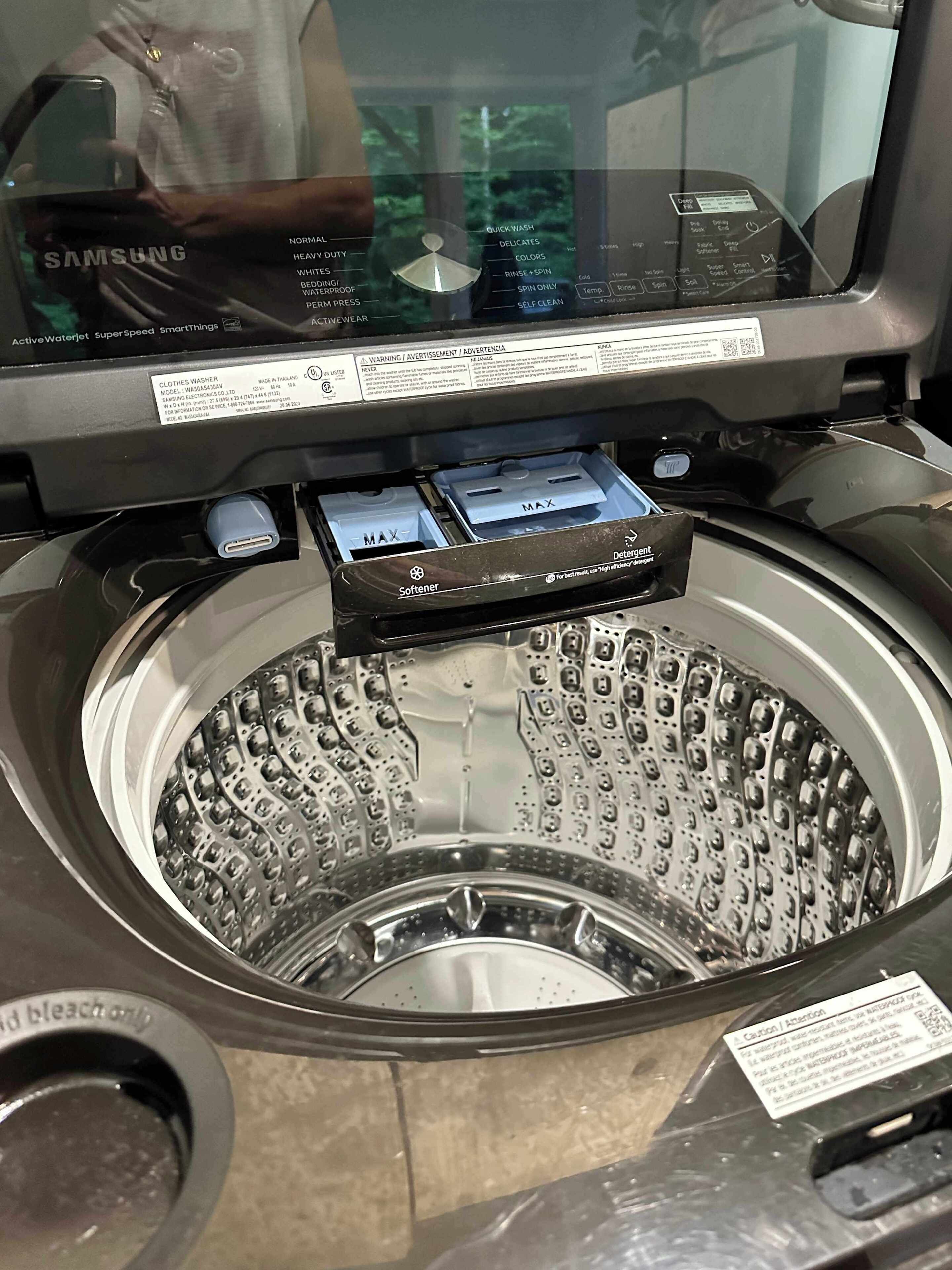 Vista frontal de una lavadora de carga frontal, con panel de control, compartimento para detergente e indicador de nivel de agua.