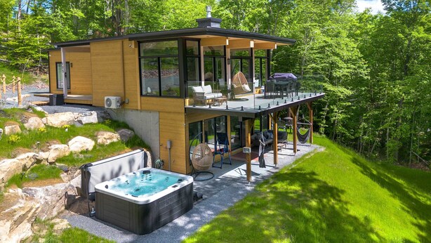 Eine moderne Hütte mit Whirlpool, Sitzgelegenheiten im Freien und einer Terrasse mit Blick auf einen bewaldeten Bereich.