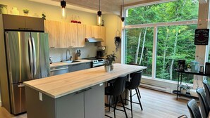 Eine moderne Küche mit einer großen Kochinsel, Edelstahlgeräten und Blick auf den Wald.