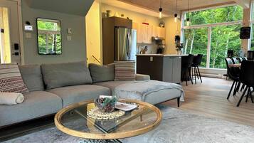 A modern living room with a sofa, a coffee table, and a view of the kitchen and dining area.