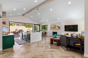 A modern kitchen with a central island, dining area with a sofa and table, and a TV mounted on the wall.