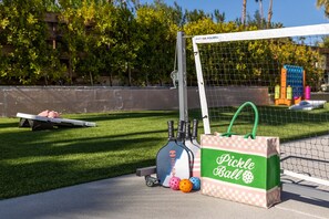 A pickleball court with a net, a bag labeled 'Pickle Ball,' and a ball cart with balls.