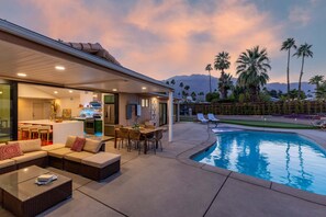 A modern outdoor living area with a pool, outdoor kitchen, and seating.