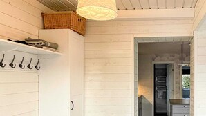 En hall med en vit vägg, en hängande lampa och en dörr som leder till ett köksområde med skåp och en bänkskiva.