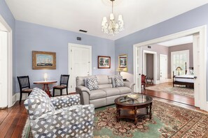 Un salon spacieux avec un canapé beige, des fauteuils à motifs, une table basse et un lustre.