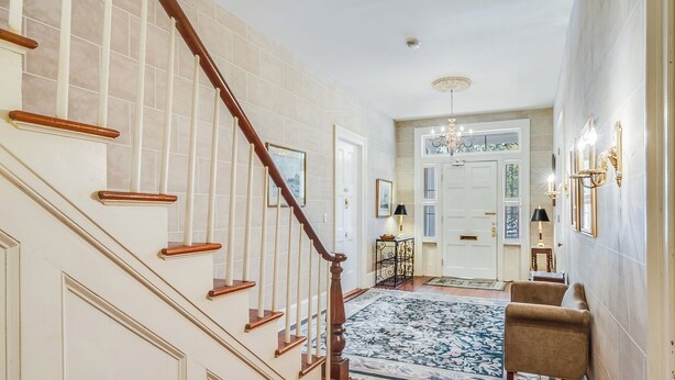 Una escalera con barandillas de madera, un tapete con diseño y una zona de estar con una silla.