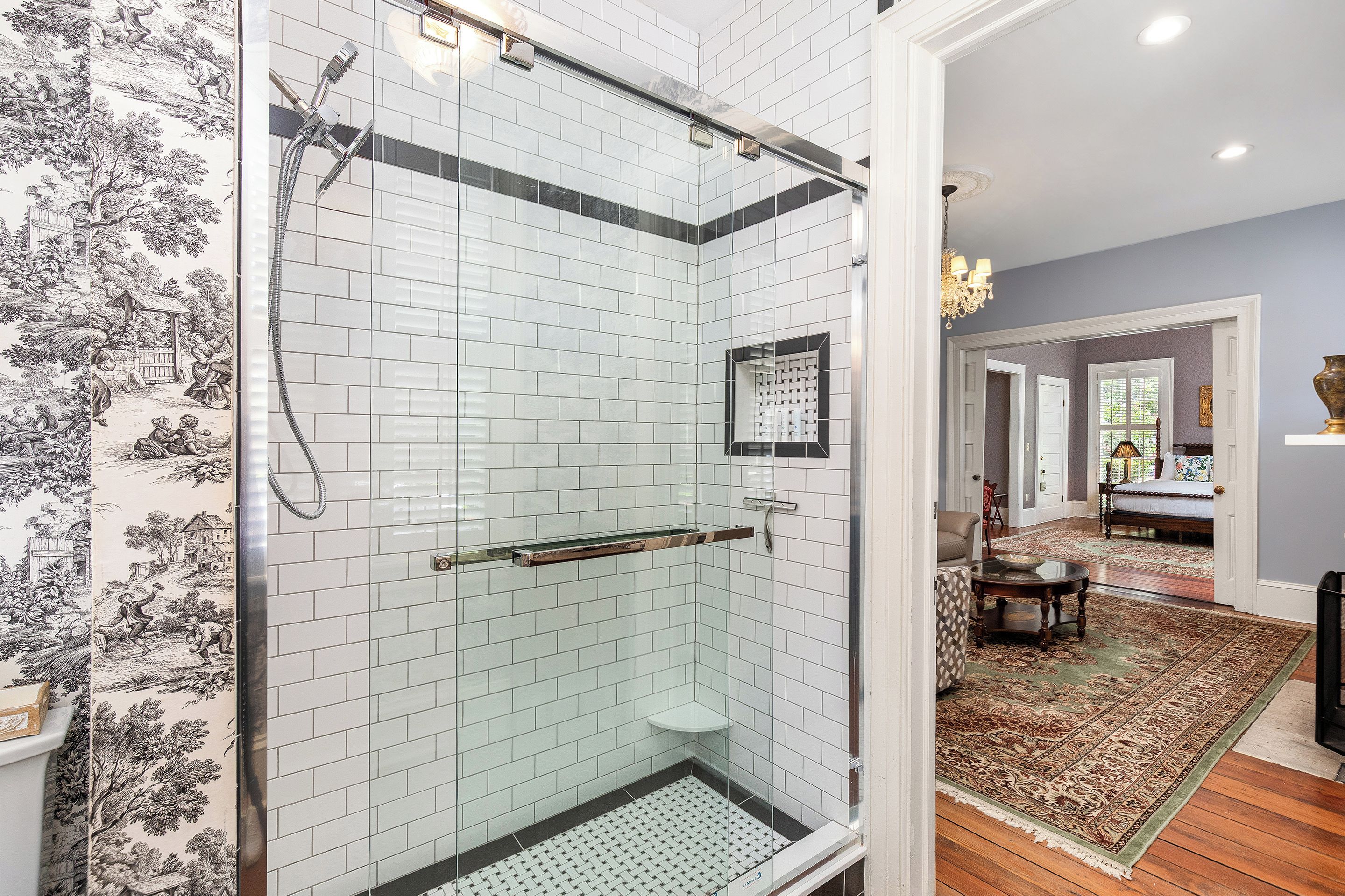 A modern bathroom with white subway tiles, a glass shower enclosure, and a patterned wall.