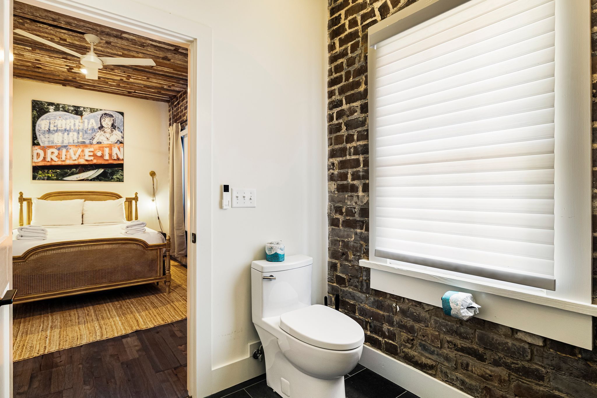 A bedroom with a bed, a white toilet, and a brick wall.
