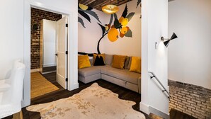 Ein modernes Wohnzimmer mit einem grauen Ecksofa, gelben Kissen, einem weißen Teppich und einer Wandmalerei mit Orangen.