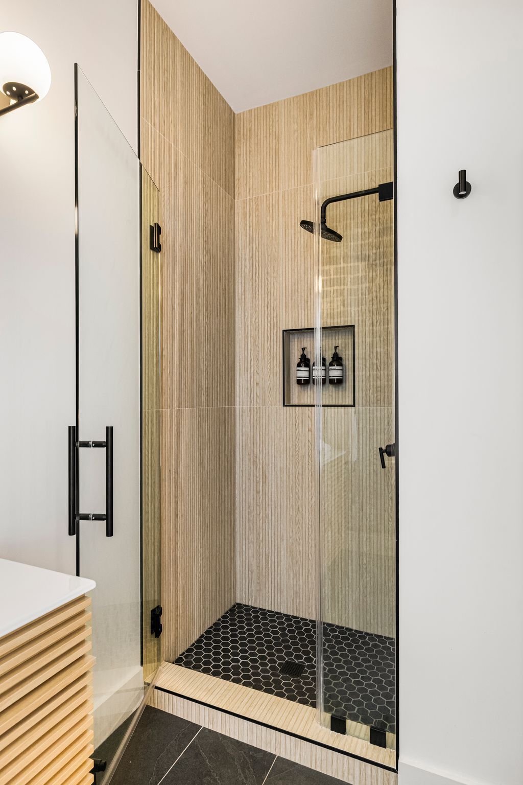 Una ducha moderna con puerta de vidrio, paneles de madera y cabezal de ducha negro.