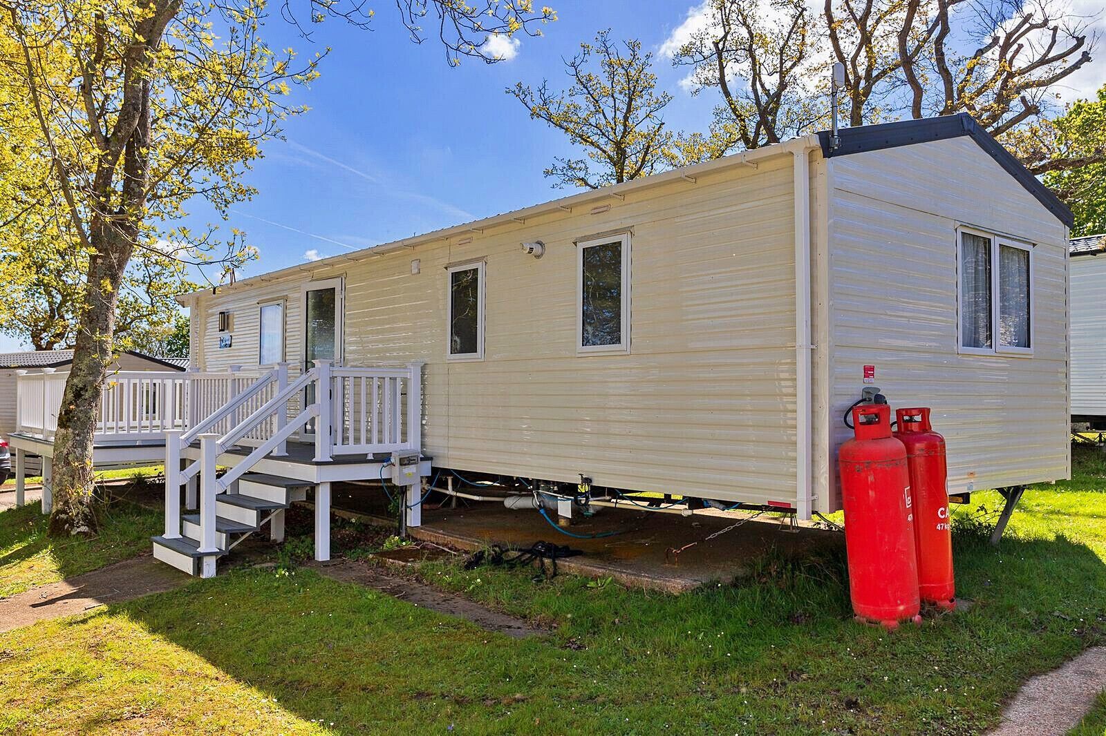 A mobile home with a porch and steps, a small deck, and two red propane tanks.