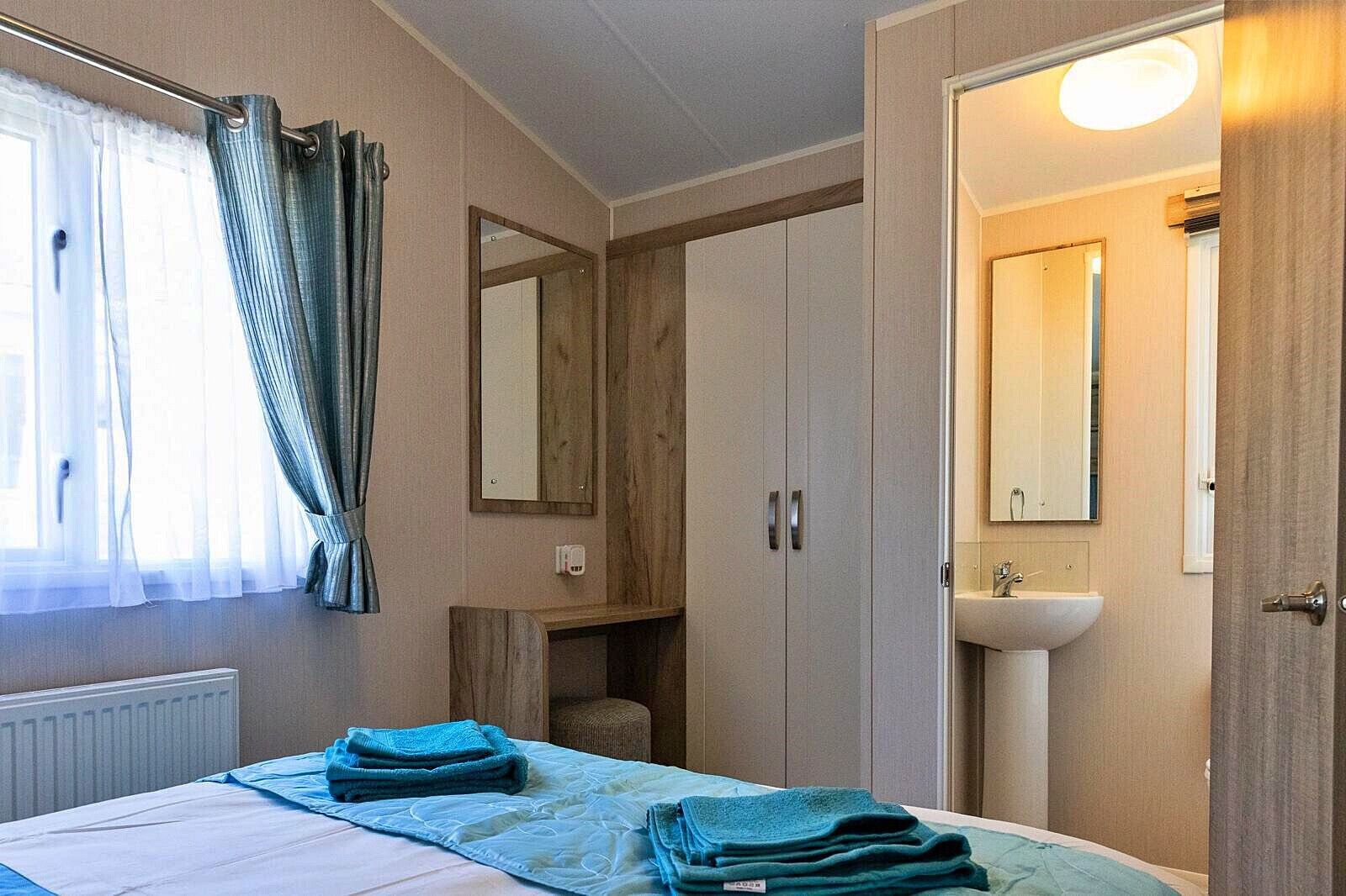 A hotel room with a bed, a bedside table, a mirror, a wardrobe, and a bathroom with a sink.