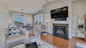 A spacious living room with a fireplace, a sofa, a coffee table, and a TV mounted above the fireplace.