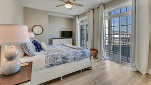 A bedroom with a bed, a TV, a ceiling fan, and large windows.