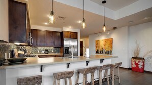 A modern kitchen with dark wood cabinets, a stainless steel refrigerator, a large island with bar stools, and pendant lighting.