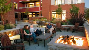 An outdoor patio with seating, a fire pit, and a brick building in the background.