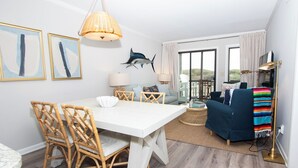 En moderne stue med spisebord, fletstole, en blå sofa og en balkon med udsigt.