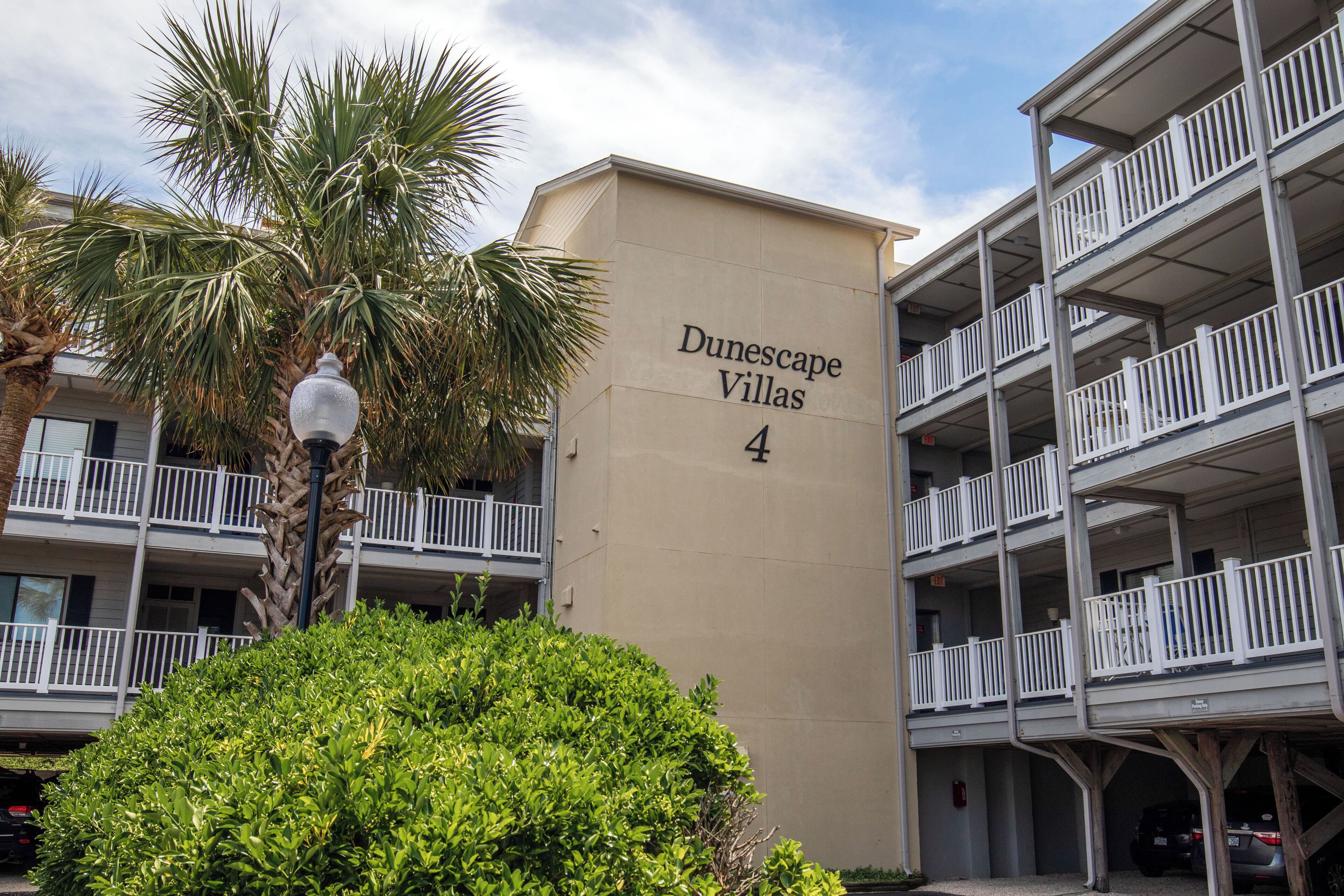 A building labeled "Dunescape Villas 4" with a multi-story structure, balconies, and a palm tree in the foreground.