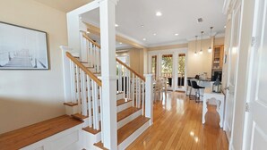 A spacious interior with a wooden staircase, a dining area, and a kitchen. - Saltwater Cottage, A Cozy Beach Club Cottage-Cottage 21- Signature Properties (Gulf Shores)