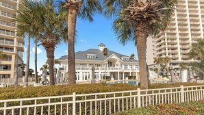 A hotel with a pool, surrounded by palm trees and a white fence. - Saltwater Cottage, A Cozy Beach Club Cottage-Cottage 21- Signature Properties (Gulf Shores)
