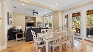 A spacious living room with a dining area, a ceiling fan, a TV, and a large sliding glass door leading to an outdoor patio. - Saltwater Cottage, A Cozy Beach Club Cottage-Cottage 21- Signature Properties (Gulf Shores)