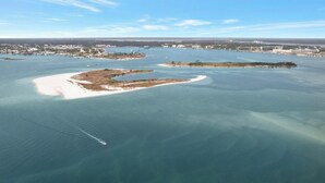 Luftaufnahme einer Küstenlandschaft mit einer weiten Wasserfläche, mehreren kleinen Inseln und einer in der Ferne liegenden Stadt.