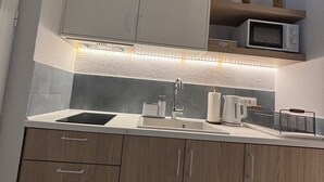 A modern kitchen with wooden cabinets, a built-in microwave, and a countertop with a kettle and a coffee maker. - Agathi Beauty Studios (Rhodes)