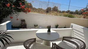 A patio with a round table and wicker chairs, surrounded by a white wall and a chain-link fence. - Agathi Beauty Studios (Rhodes)