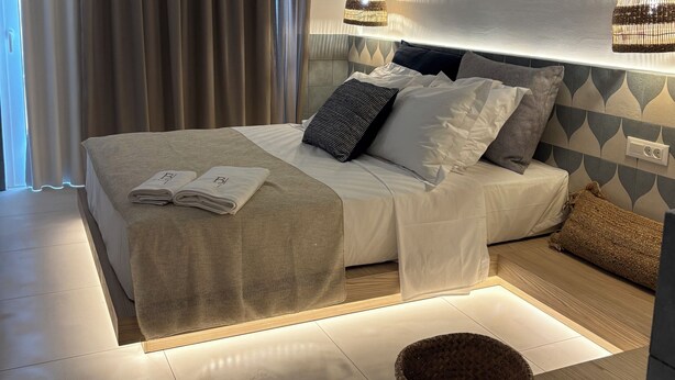 A modern bedroom with a large bed, two hanging lamps, and a view of the outdoors through sheer curtains. - Agathi Beauty Studios (Rhodes)