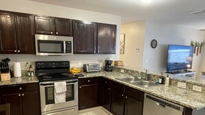A modern kitchen with dark wood cabinets, stainless steel appliances, a granite countertop, and a built-in dishwasher. - Stylish Home in Duval w/Granite, Tile Floors, Glass Lanai & Gas Golf Cart! (The Villages)