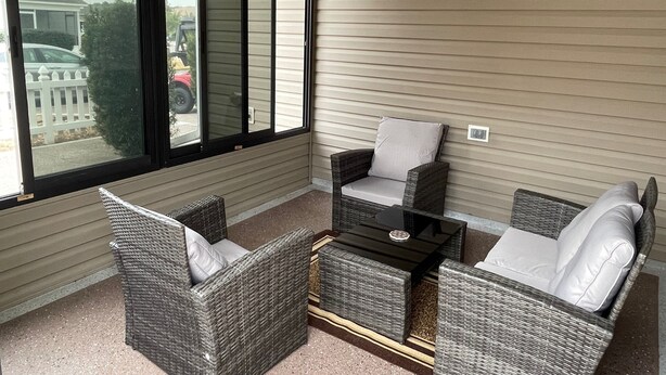 A balcony with wicker furniture, a glass table, and a view of a residential area. - Stylish Home in Duval w/Granite, Tile Floors, Glass Lanai & Gas Golf Cart! (The Villages)