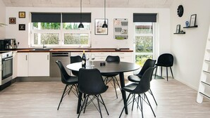 A modern kitchen with white cabinets, a dining table with black chairs, and a window with a view of greenery. - 4 Star Holiday Home in Borkop (Borkop)