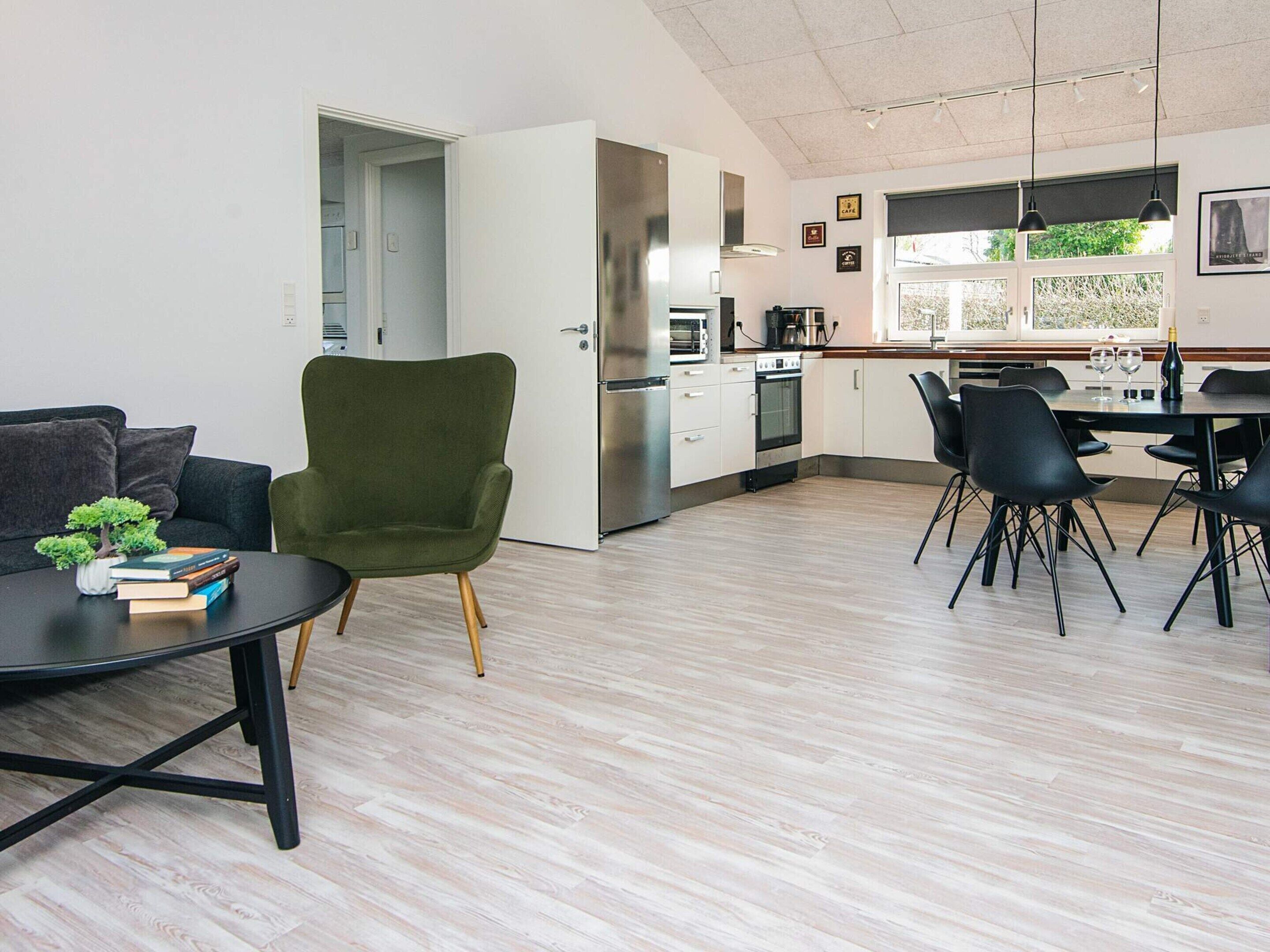Una cocina moderna con armarios blancos, horno integrado y una zona de comedor con sillas negras y una mesa.