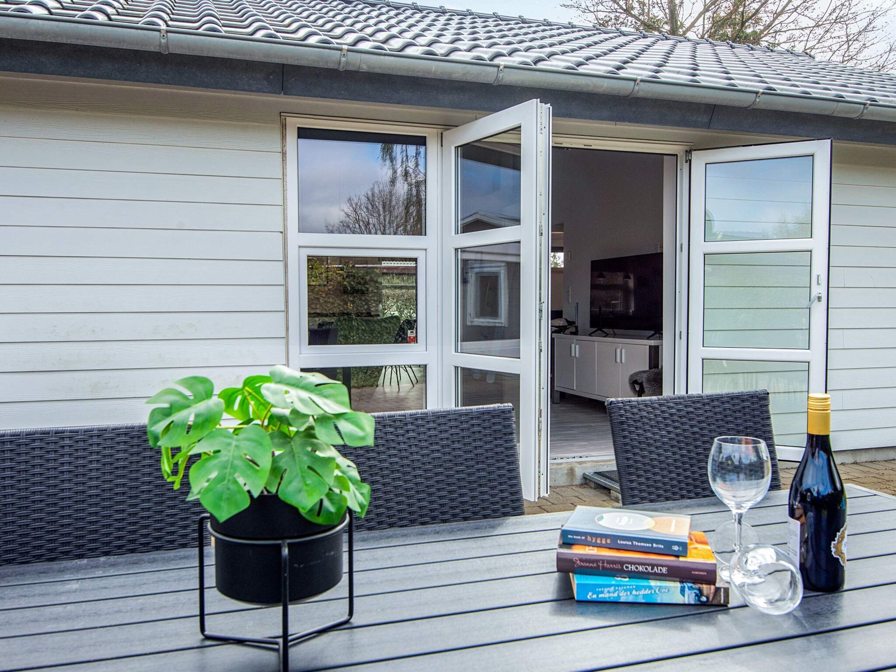 Uma área externa com mesa, planta em vaso, garrafa de vinho e livros.