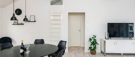 A modern living space with a dining area featuring a round table and chairs, a television on a cabinet, and a plant.